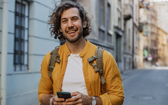 Een jonge man glimlacht terwijl hij een telefoon vasthoudt