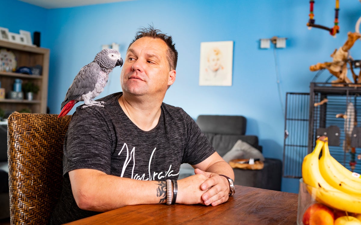 Manfred Roubos zit aan tafel met een papegaai op zijn schouder