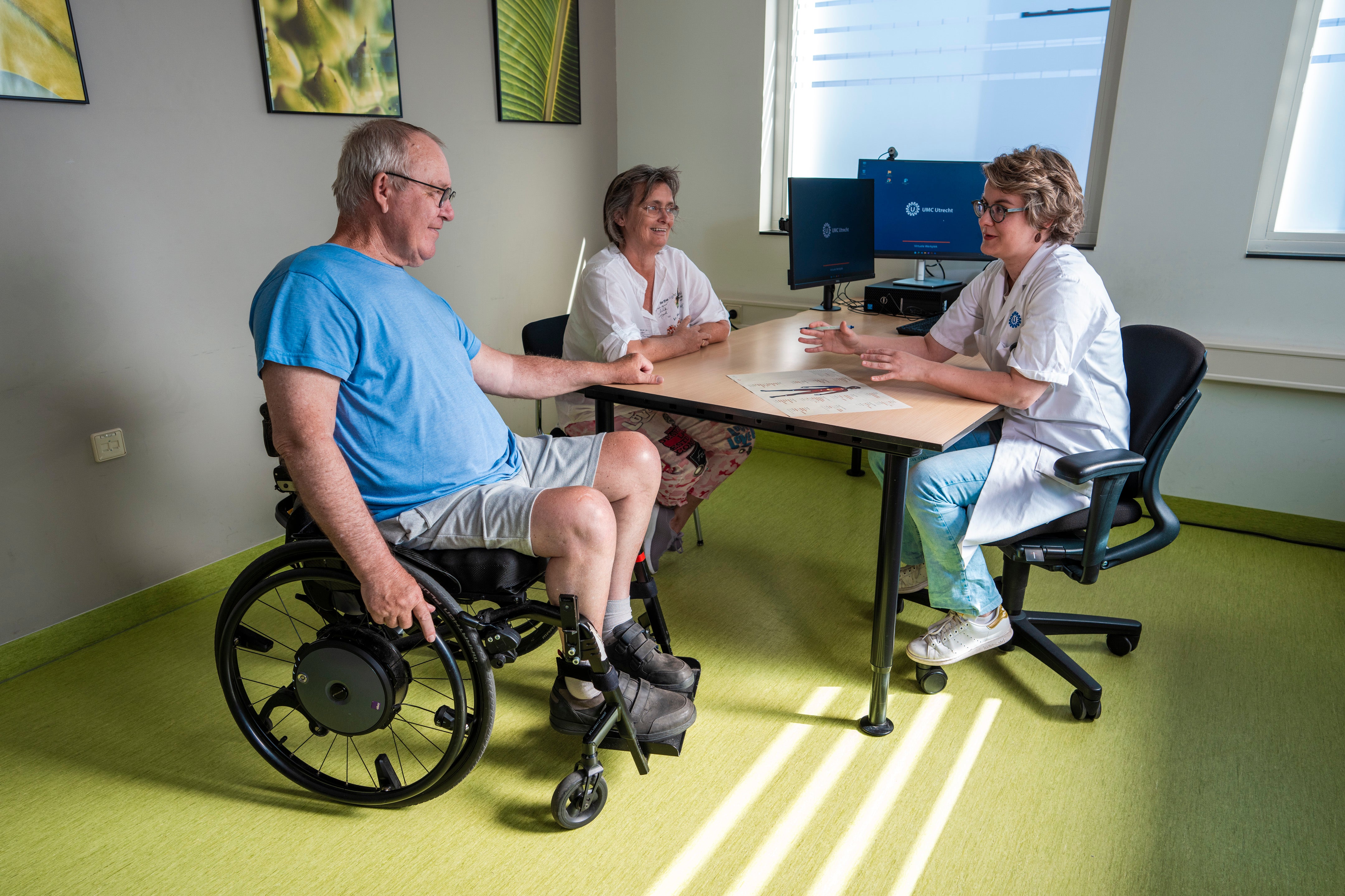 Patiënt met spierziekte in rolstoel spreekt met arts in spreekkamer
