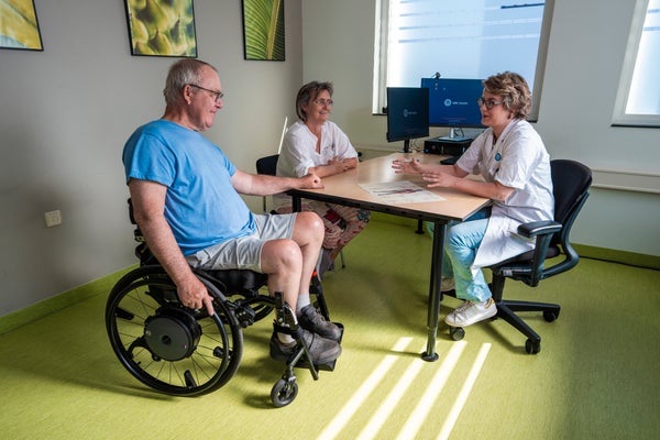 Patiënt met spierziekte in rolstoel spreekt met arts in spreekkamer