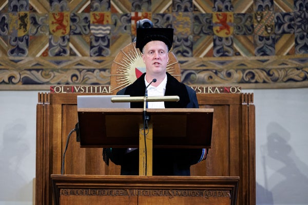 Een man met een afstudeercap en toga staat op een podium