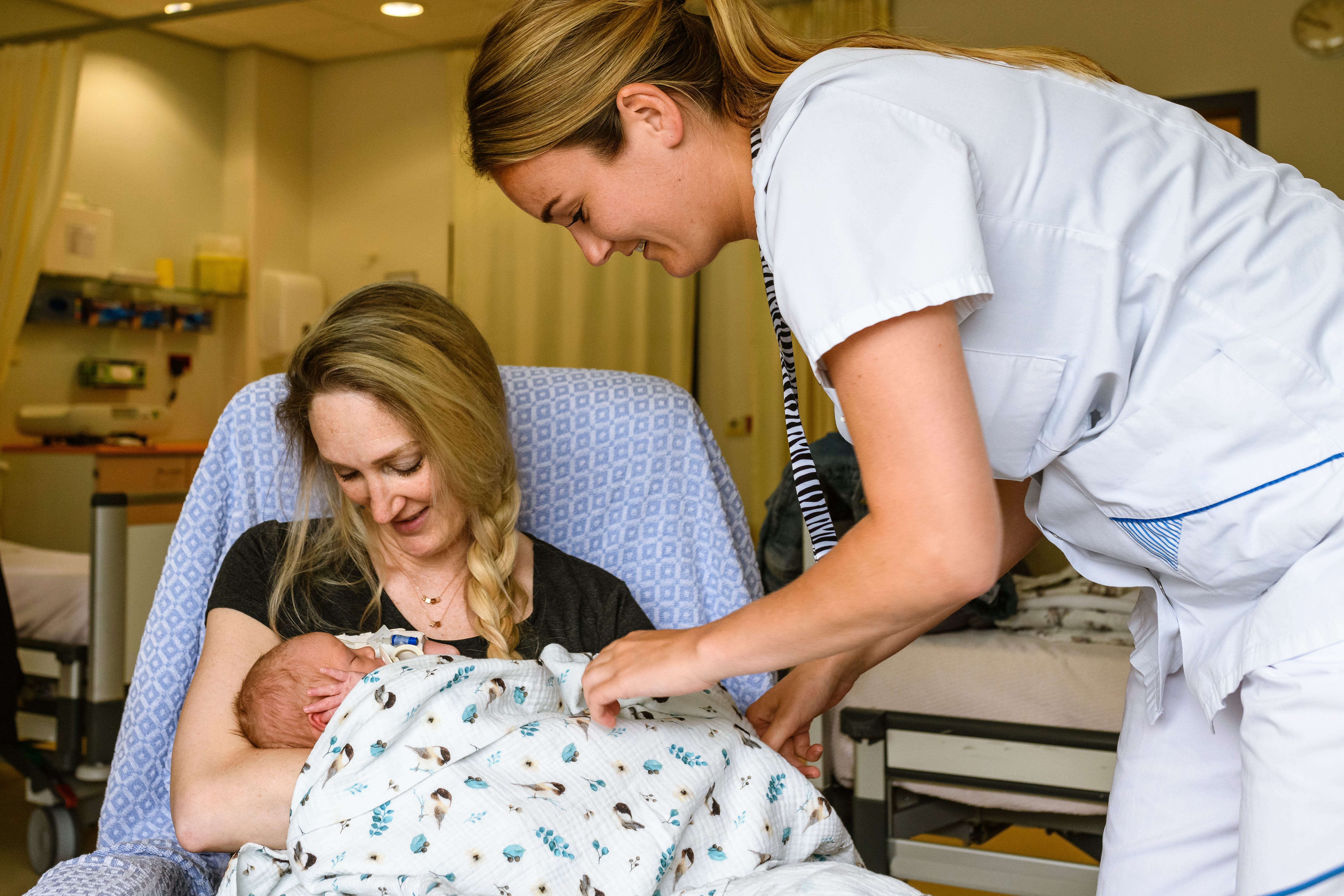 Een moeder met een baby op schoot wordt geholpen door een verpleegkundige.