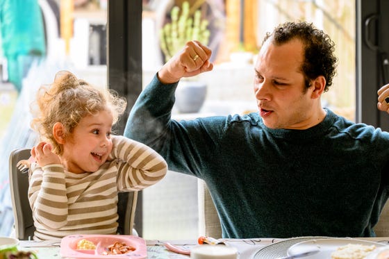 Kind eet aan tafel met een man naast haar die juicht