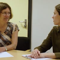 Een vrouw zit aan een tafel met een vrouw die een klembord vasthoudt