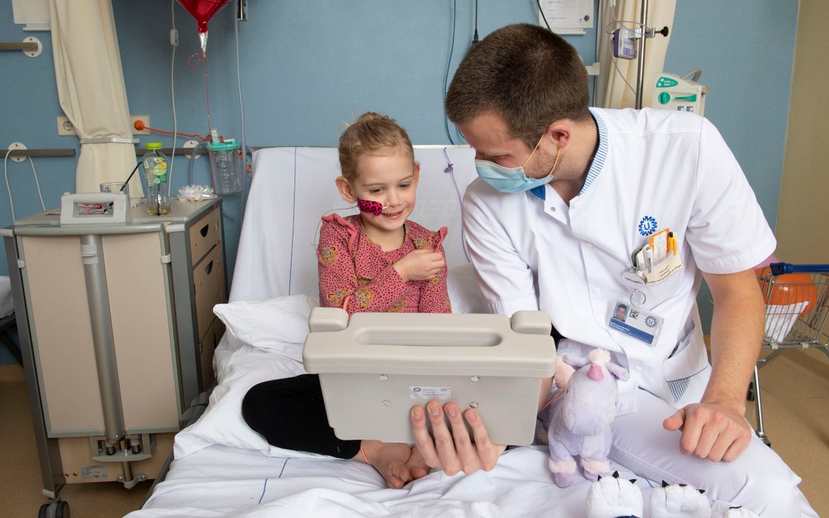 Meisje en zorgverlener zitten op een ziekenhuisbed en kijken naar een tablet.