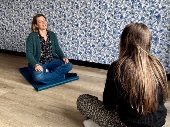 Twee vrouwen zitten op een matje op de grond. Mindfulness kan onderdeel zijn van het herstelaanbod psychiatrie.