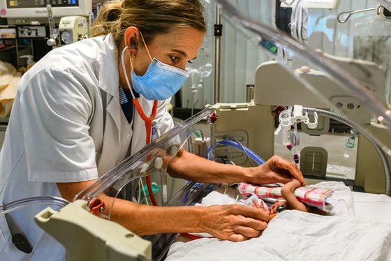 Een baby in een couveuse die wordt onderzocht door een vrouwelijke neonatoloog.