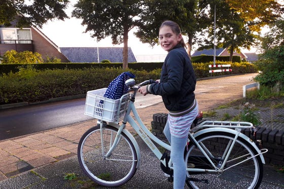 Een meisje op een fiets met een blauwe tas in een witte mand