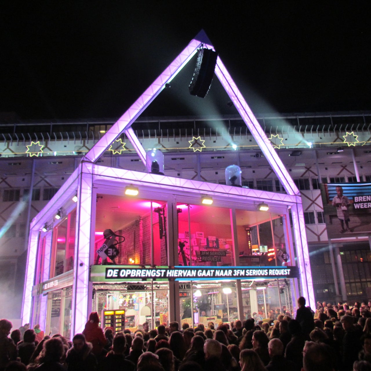 Het Glazen Huis van 3FM Serious Request in de nacht met een massa mensen eromheen.