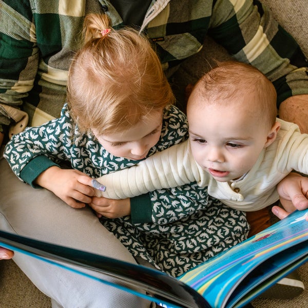 Emma en Thomas lezen een boekje bij hun vader op schoot