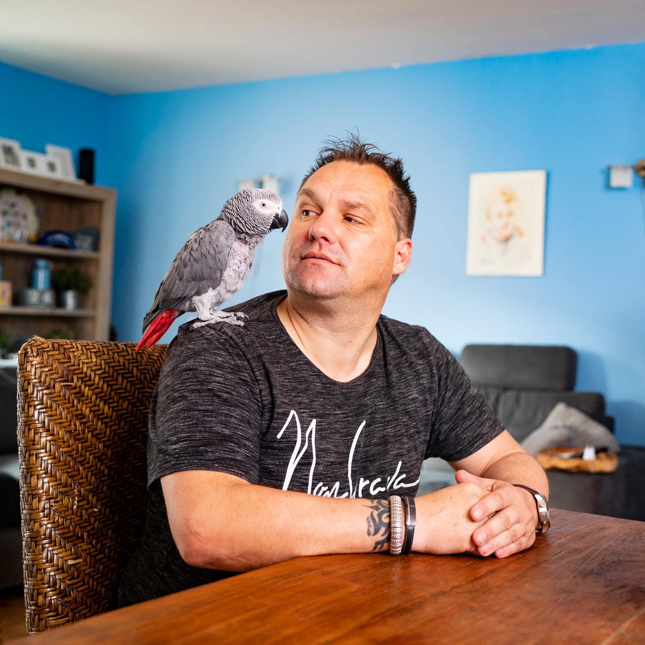 Manfred Roubos zit aan tafel met een papegaai op zijn schouder