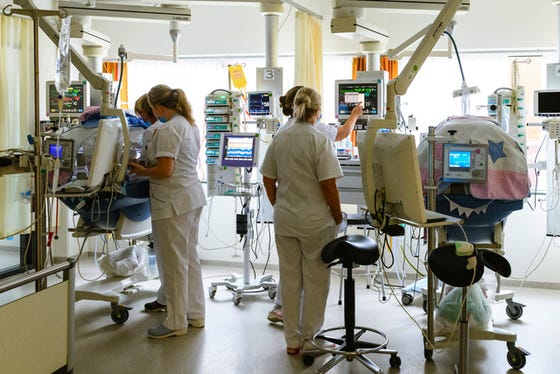 Foto gemaakt op de NICU, meerdere babybedden, zorgverleners en apparatuur.