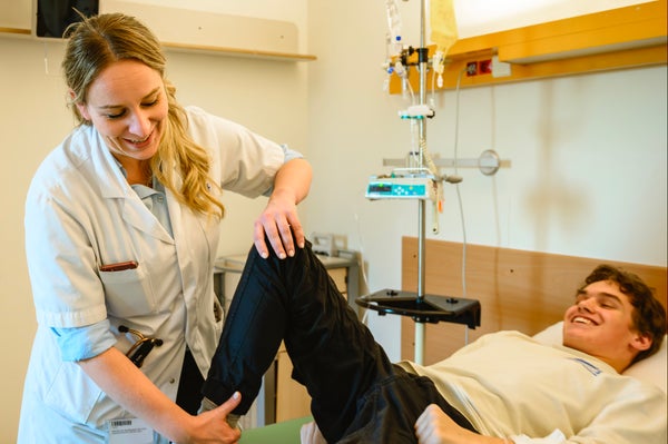 Fay-Lynn in een witte jas en wit shirt die iemands been vasthoudt