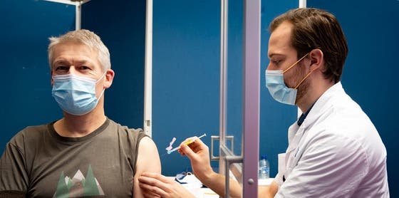 Een man met een mondneusmasker geeft een injectie aan een dokter