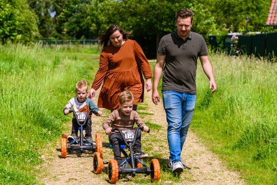 Twee ouders lopen door grasveld met twee kinderen op skelters